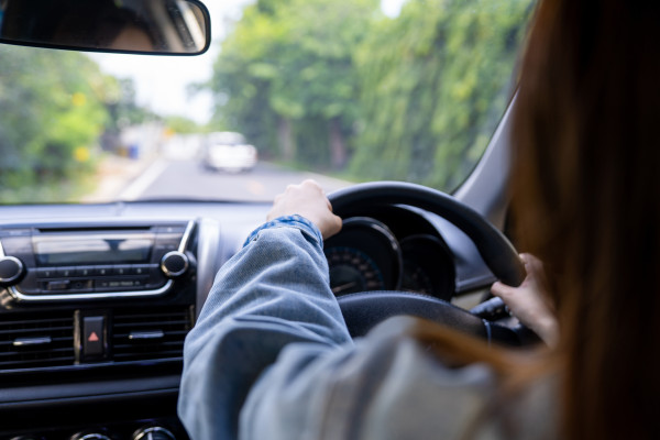 View of a woman driving down the road, image taken from backright seat